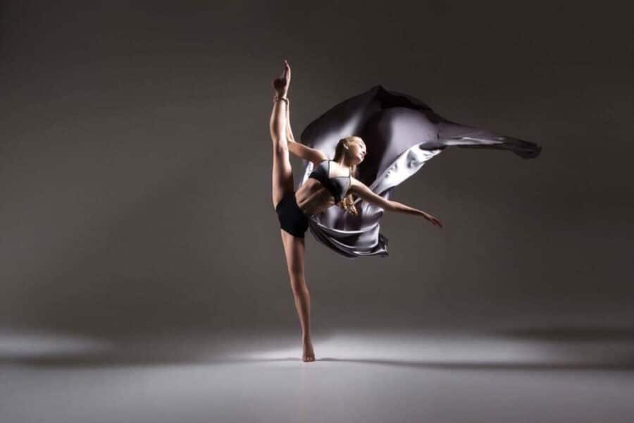Dancer in a high leg extension with flowing grey fabric